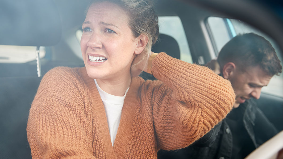 Upset couple inside car after crash, woman showing pain and man looking distressed in a tense moment.