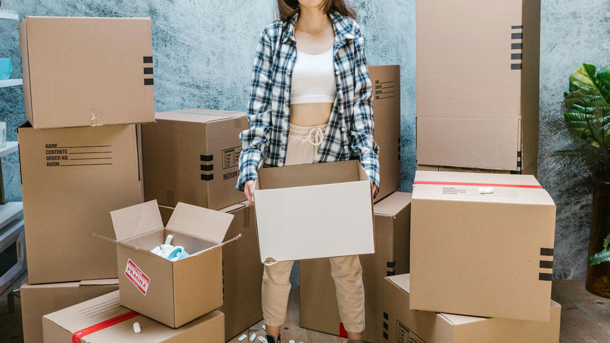 Woman holding empty cardboard box surrounded by packed boxes, reflecting family hard times and unresolved humiliation feelings.