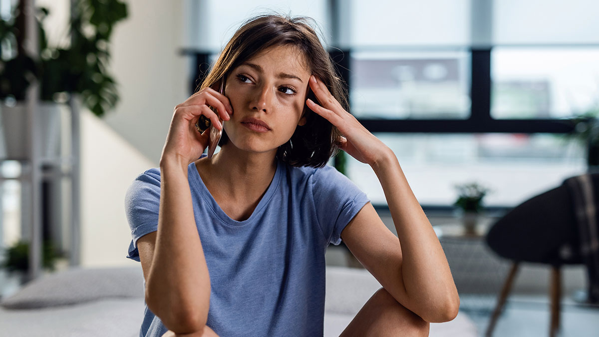 Young woman in a blue shirt looking confused while talking on the phone about childcare for nine kids.