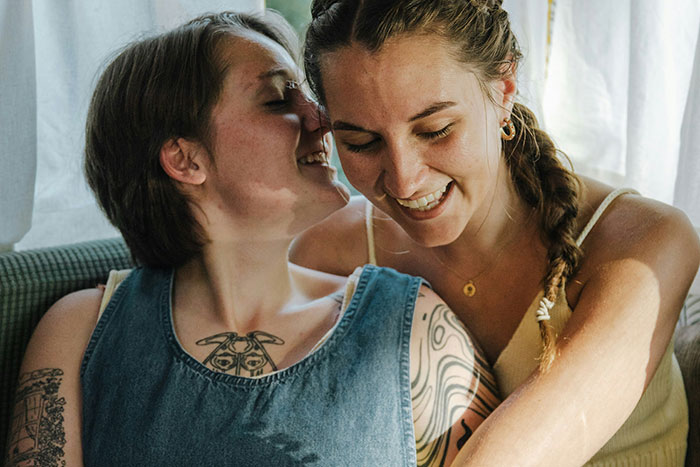 A woman whispers to her smiling stepdaughter, highlighting tension around stepdaughter’s sexuality during Thanksgiving. A woman whispers to her smiling stepdaughter, highlighting tension around stepdaughter’s sexuality during Thanksgiving.