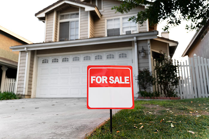 For sale sign in front of suburban house as woman considers selling home due to messy mooching adult stepkids