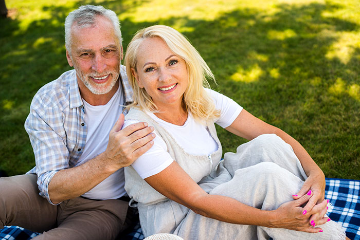 Middle-aged woman and man sitting on a picnic blanket outdoors, reflecting on messy adult stepkids and selling the house.