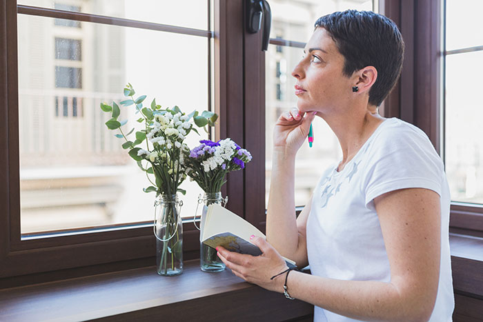 Woman holding a book, sitting by a window, thoughtfully planning a walk home with daughter or friend. Woman holding a book, sitting by a window, thoughtfully planning a walk home with daughter or friend.