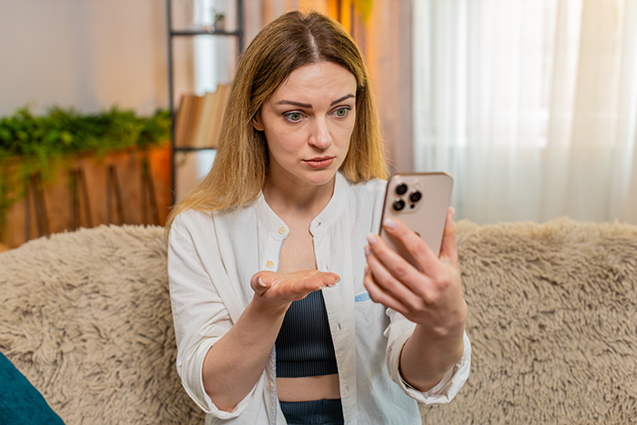 Woman looking frustrated at her smartphone while sitting on a couch, relating to a car borrowing dispute story.