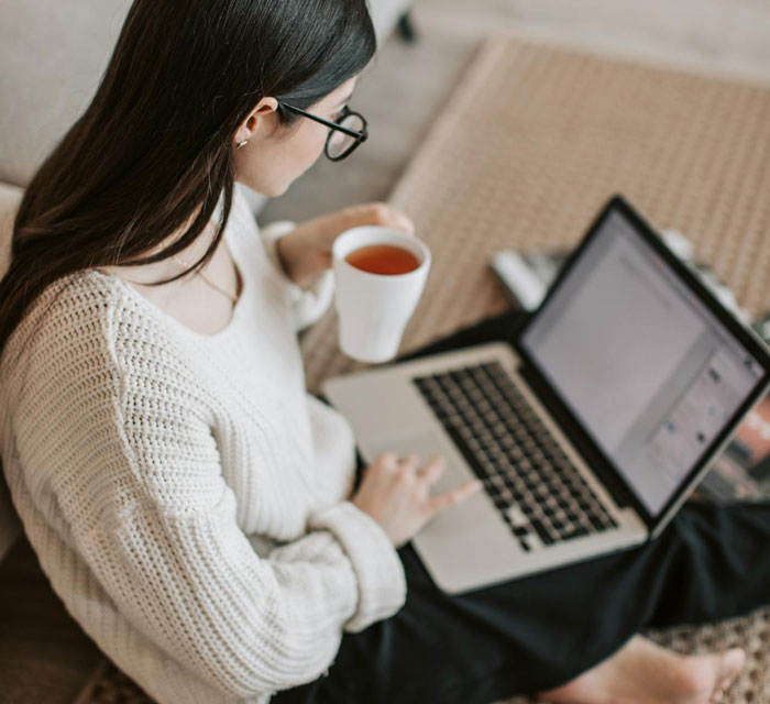 Woman wearing glasses and a white sweater working on a laptop while holding a cup, related to stealing and publishing a book incident.