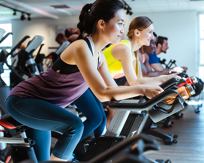 Group of people wearing activewear cycling indoors with focus on woman, illustrating trending activewear in public debate. Group of people wearing activewear cycling indoors with focus on woman, illustrating trending activewear in public debate.