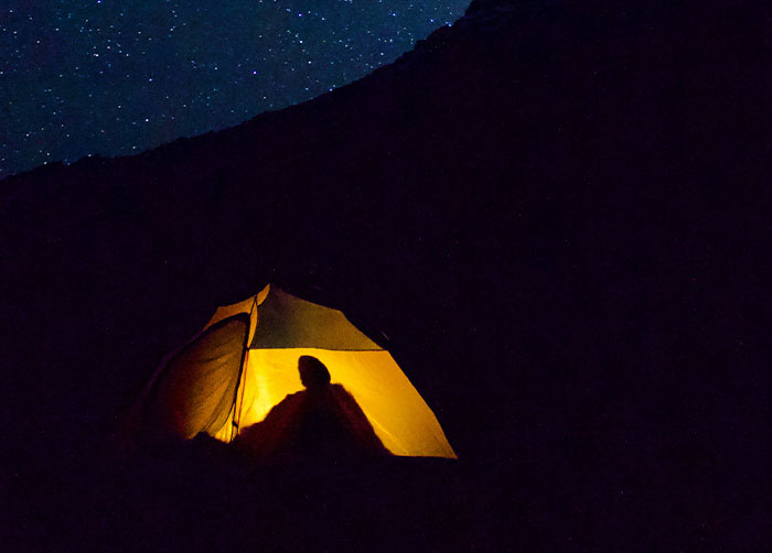 Person silhouetted inside glowing tent at night under starry sky, illustrating worst night’s sleep in an outdoor place.