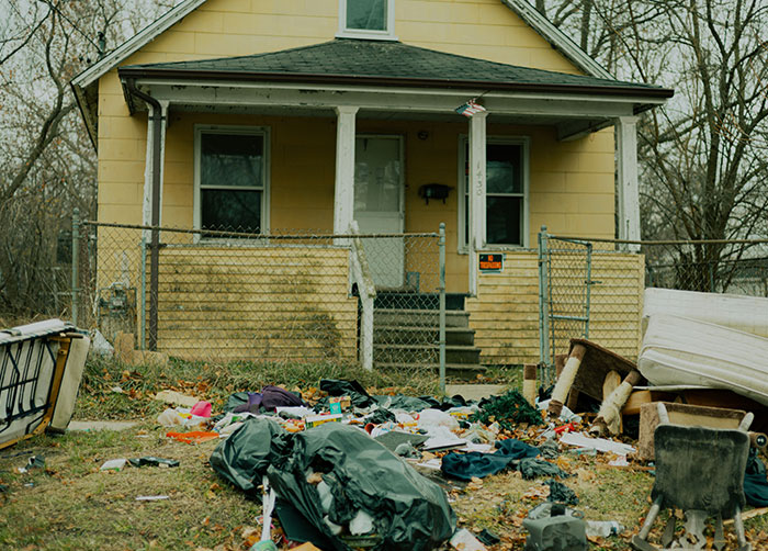 Yard cluttered with trash and old furniture outside a yellow house, illustrating worst night’s sleep due to location.