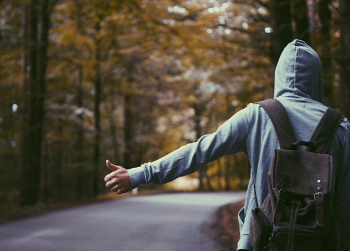 Person in a hoodie with a backpack hitchhiking on a forest road, illustrating worst night’s sleep in a challenging place.