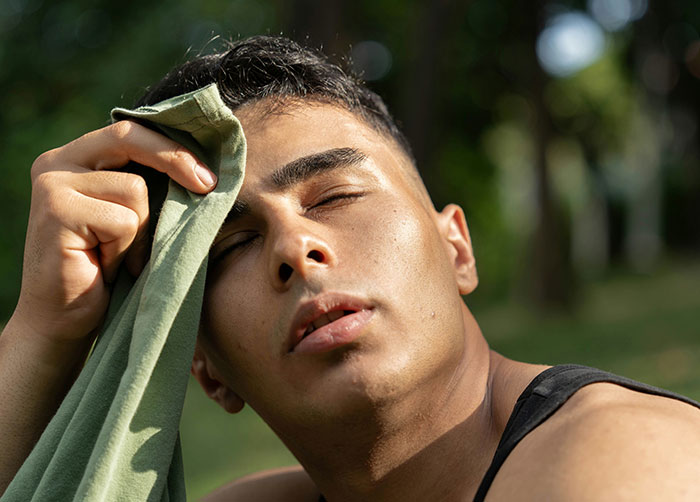 Man wiping sweat from forehead outdoors, showing discomfort that could cause the worst night’s sleep due to place conditions