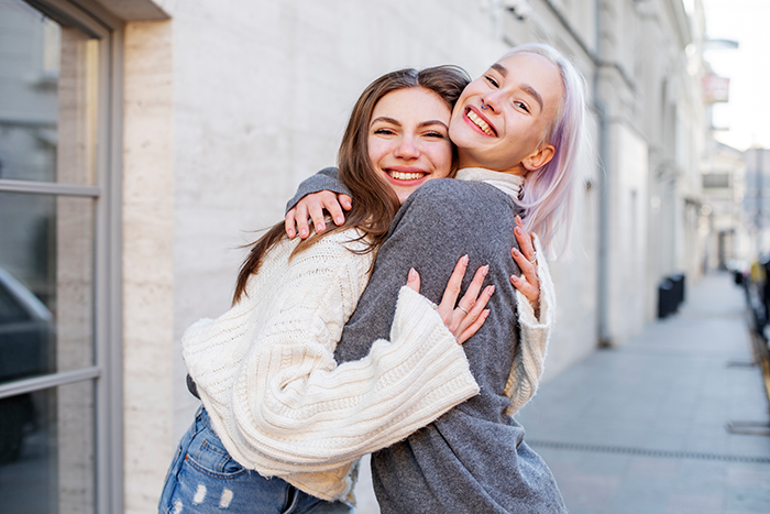 Two women smiling and hugging outdoors, highlighting cousin's family accusing woman of stealing spotlight with baby and ring. Two women smiling and hugging outdoors, highlighting cousin's family accusing woman of stealing spotlight with baby and ring.