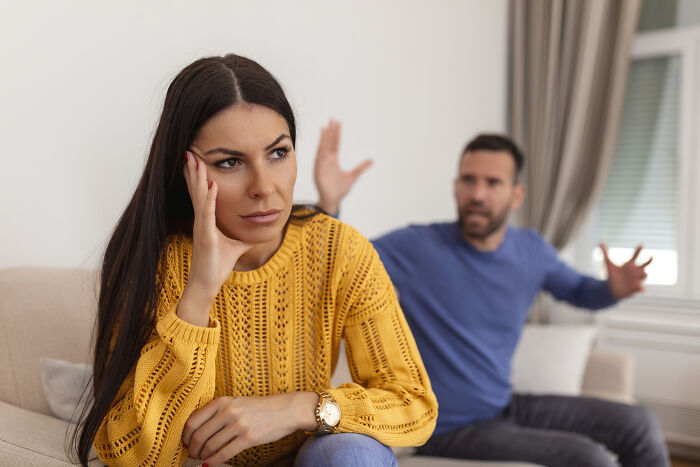 Frustrated woman sitting with hand on face while man in background gestures angrily, reflecting regret of having kids.