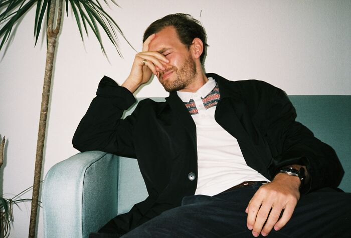 Man in black jacket sitting on sofa with hand on face, expressing regret and frustration about having kids.