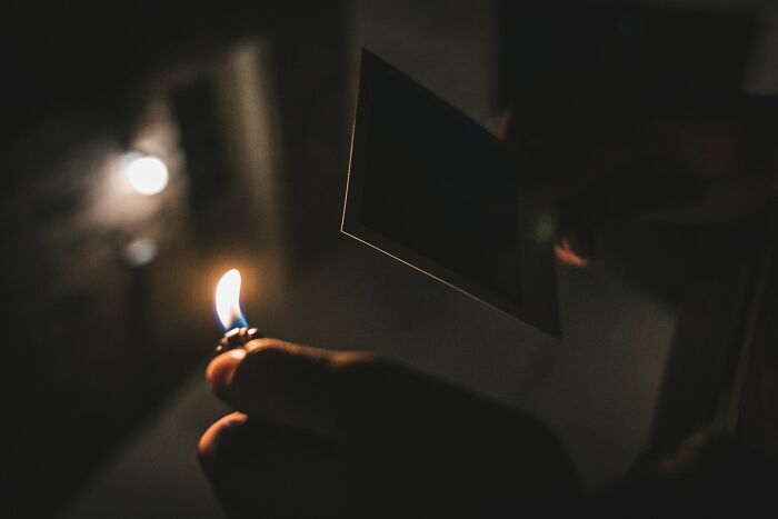Person holding a lit lighter close to a photo in dim light, symbolizing struggle and insensitive cancer comments.