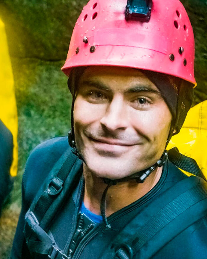 Zac Efron wearing a red helmet and outdoor gear smiling during an adventurous activity in a natural setting. Zac Efron wearing a red helmet and outdoor gear smiling during an adventurous activity in a natural setting.