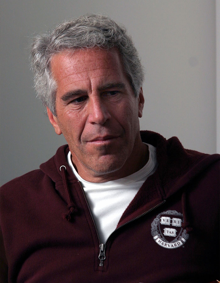 Jeffrey Epstein in a maroon Harvard sweatshirt, looking down pensively, linked to disturbing desk photo backlash after estate images release.
