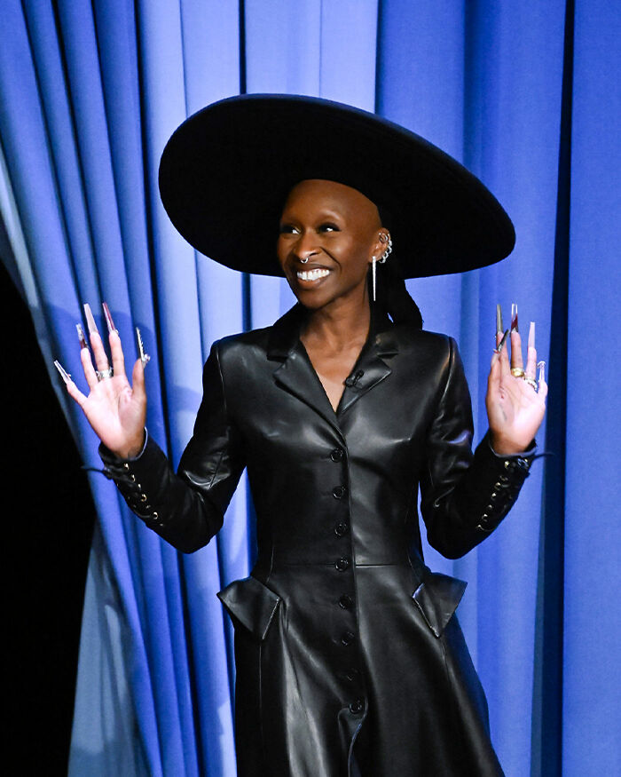 Cynthia Erivo wearing a black leather outfit and large hat, showing her oddly large hands during a public appearance. Cynthia Erivo wearing a black leather outfit and large hat, showing her oddly large hands during a public appearance.