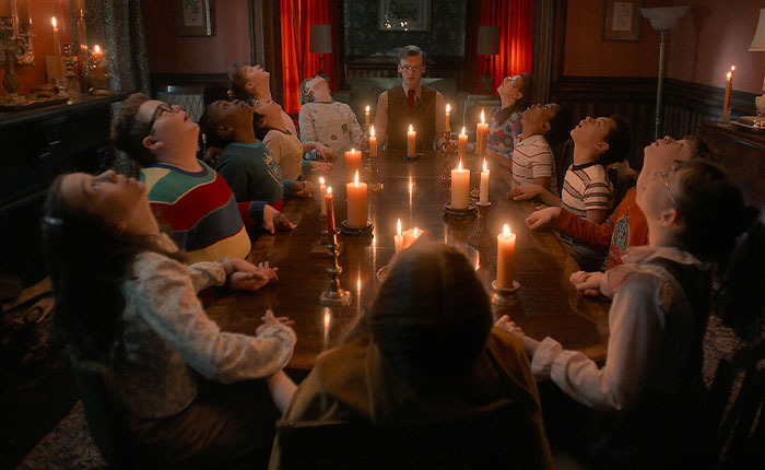 Group of children and a man sitting around a candlelit table in a dark room, Stranger Things 5 scene with eerie atmosphere. Group of children and a man sitting around a candlelit table in a dark room, Stranger Things 5 scene with eerie atmosphere.