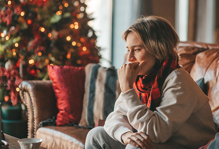 Young woman sitting on a couch looking thoughtful during a Christmas gathering in a cozy living room decorated for the holiday season. Young woman sitting on a couch looking thoughtful during a Christmas gathering in a cozy living room decorated for the holiday season.