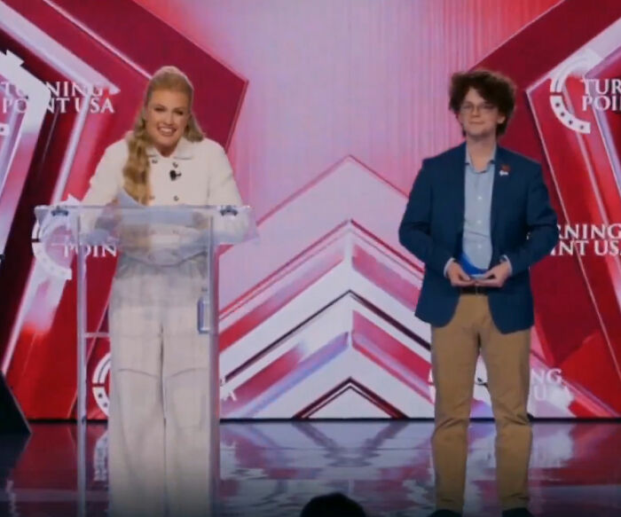 Erika Kirk speaking at TPUSA event, smiling at podium with red and white backdrop, viral Freudian slip moment captured. Erika Kirk speaking at TPUSA event, smiling at podium with red and white backdrop, viral Freudian slip moment captured.