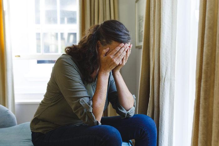 Woman sitting indoors covering her face in distress, reflecting tension over nephew calling her mom and family conflict.