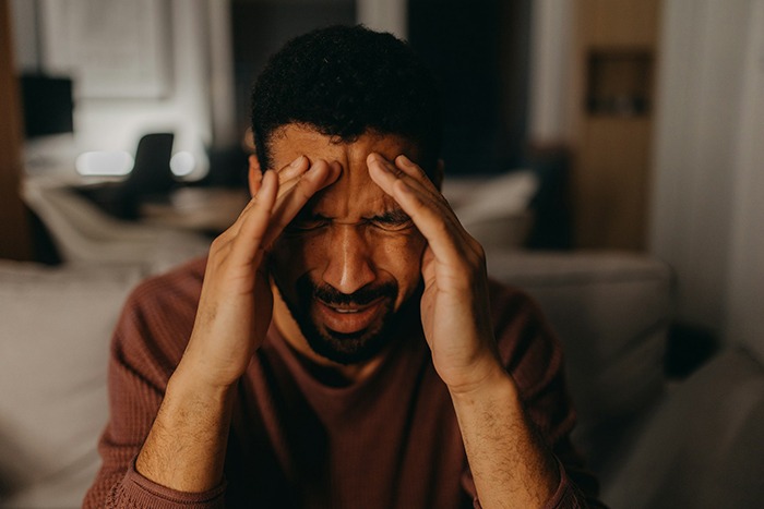 Man in brown sweater sitting indoors, holding his head in distress, illustrating family intervention and uncomfortable truth. Man in brown sweater sitting indoors, holding his head in distress, illustrating family intervention and uncomfortable truth.