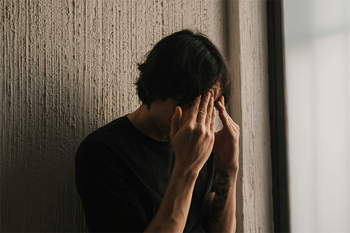 Teen boy sitting alone in a dim room, covering his face showing fear and distress related to violent sister and family issues. Teen boy sitting alone in a dim room, covering his face showing fear and distress related to violent sister and family issues.