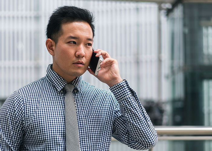 Man takes a call in Korean outdoors, wearing a checkered shirt and tie, with a focused expression on his face. Man takes a call in Korean outdoors, wearing a checkered shirt and tie, with a focused expression on his face.