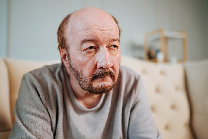Older man with a serious expression sitting on a couch, reflecting themes of marriage issues and banned family members. Older man with a serious expression sitting on a couch, reflecting themes of marriage issues and banned family members.