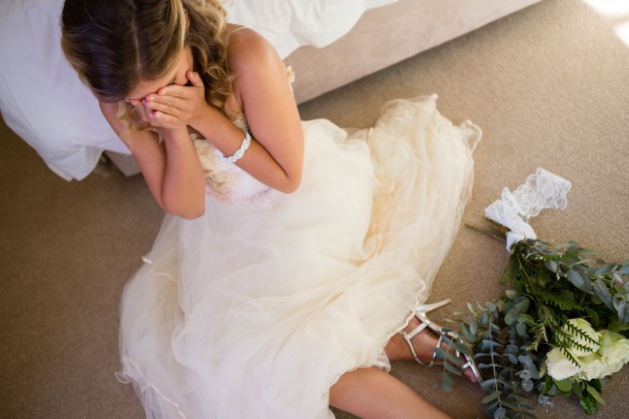 Bride in wedding dress sitting on floor upset, symbolizing husband not standing up to his mother and wife considering walking away.