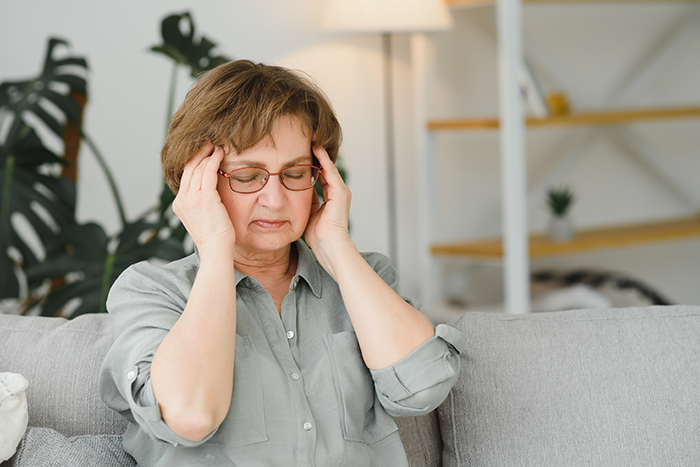 Stressed middle-aged woman sitting on couch, holding head with hands, depicting family conflict over childcare options. Stressed middle-aged woman sitting on couch, holding head with hands, depicting family conflict over childcare options.