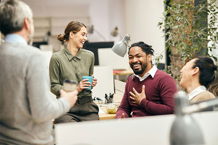 Office employees laughing and chatting during a break, highlighting employee pushback against vegan-only club beef debate. Office employees laughing and chatting during a break, highlighting employee pushback against vegan-only club beef debate.