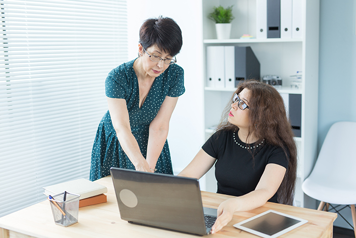 Middle-aged woman discussing wedding illustration plan with younger woman at computer, artist catching on to MIL’s plan.
