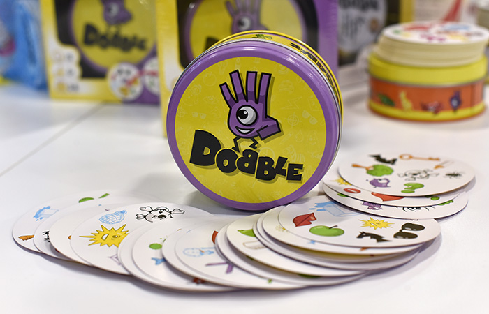 Dobble party game tin and illustrated cards spread out on a white surface, a popular choice for best party game.