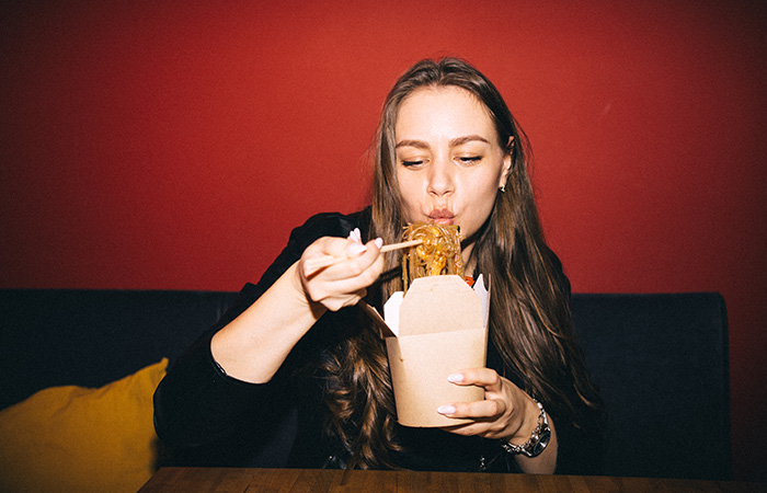 Young woman enjoying noodles with chopsticks in a casual setting, highlighting traits men find attractive in women.