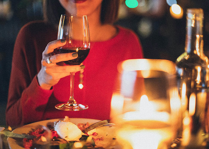 Person in a red sweater holding a wine glass during a candlelit dinner, illustrating luxury industries and luxury rip-offs.