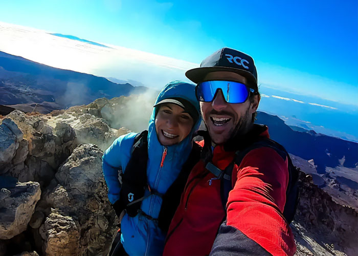 Couple hiking on Austrian mountain summit with rocky terrain and expansive sky, linked to boyfriend who abandoned woman story.