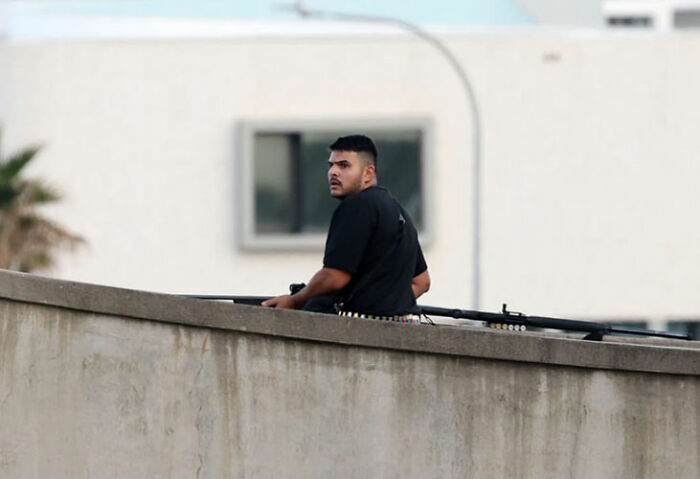 Man holding long gun behind concrete wall, related to Bondi Beach hero disarming attacker during Hanukkah event. Man holding long gun behind concrete wall, related to Bondi Beach hero disarming attacker during Hanukkah event.