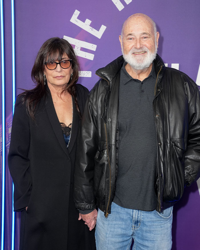 Rob Reiner at public event wearing black leather jacket beside woman in black coat with sunglasses.