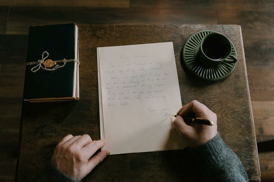 Person writing a heartfelt good morning message to my love on paper with coffee and a wrapped journal on wooden table. Person writing a heartfelt good morning message to my love on paper with coffee and a wrapped journal on wooden table.