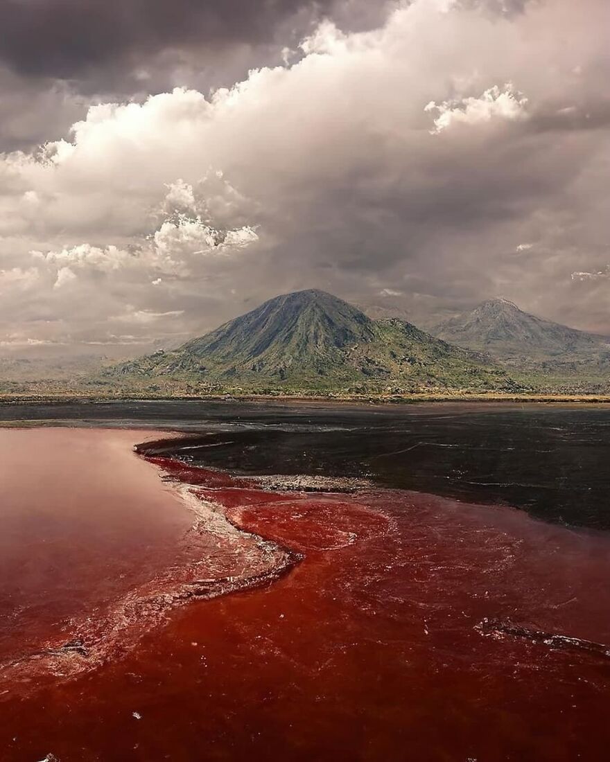 Blood-red lake with volcanic mountains under a stormy sky in one of the most dangerous places in the world to visit.