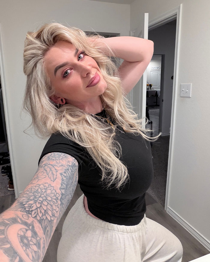 Woman with long blonde hair and tattoos taking a selfie indoors, related to man punished for not switching seats on flight controversy.