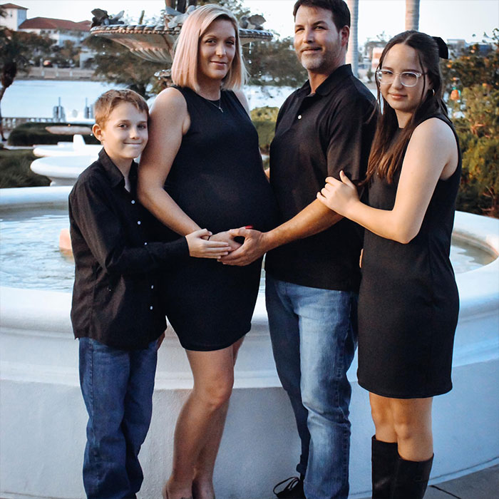 Family by a fountain during sunset with man involved in heated NFL argument holding pregnant woman's belly.