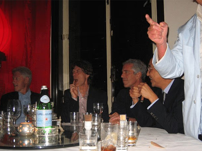 Jeffrey Epstein and others seated at a table with drinks as chilling toddler's foot is visible beside Epstein in photo. Jeffrey Epstein and others seated at a table with drinks as chilling toddler's foot is visible beside Epstein in photo.
