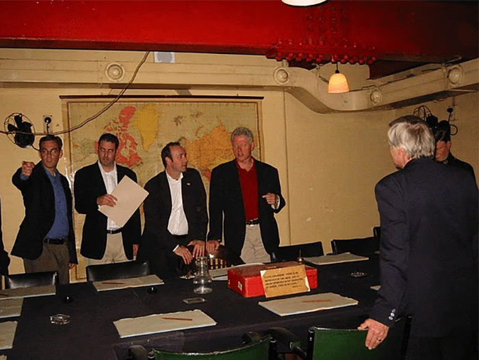 Group of men in a room with a map on the wall and a toddler's foot chillingly visible near Epstein in the photo. Group of men in a room with a map on the wall and a toddler's foot chillingly visible near Epstein in the photo.