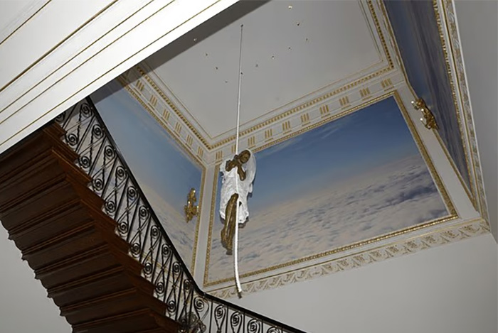 Staircase with ornate railing and ceiling mural showing a hanging sculpture resembling a chilling toddler's foot. Staircase with ornate railing and ceiling mural showing a hanging sculpture resembling a chilling toddler's foot.