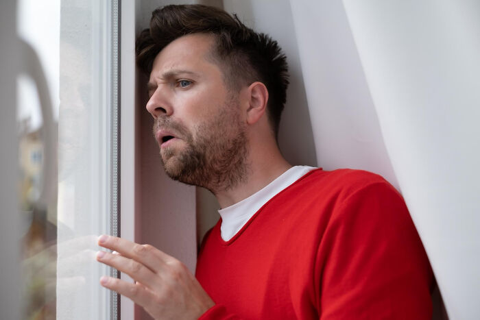Man in red sweater looking surprised while peering through a neighbor’s window, capturing bizarre things seen through windows.