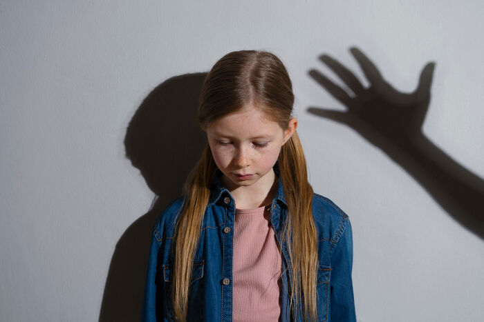 Young girl looking down sadly with a large dramatic shadow hand behind her symbolizing family drama conflicts.