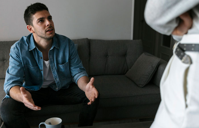 Man sitting on couch looking frustrated while confronting standing woman about fiction lowering IQ in living room. Man sitting on couch looking frustrated while confronting standing woman about fiction lowering IQ in living room.