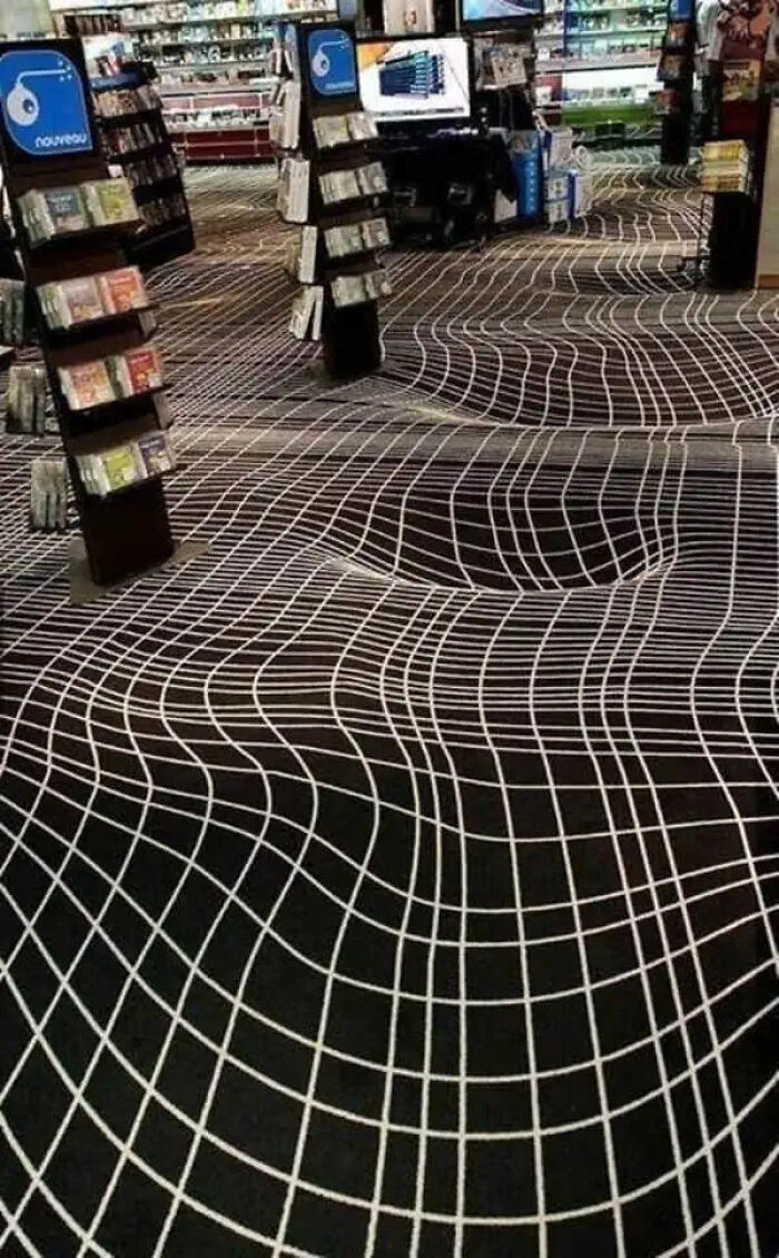 Bookstore interior with a trippy floor design featuring warped grid lines creating an illusion of depth and movement.